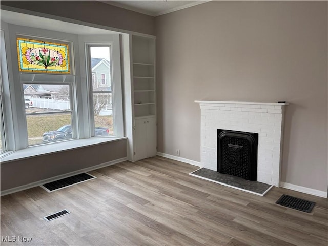 unfurnished living room with a brick fireplace, baseboards, visible vents, and wood finished floors