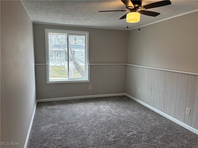 carpeted empty room featuring a wainscoted wall, crown molding, a ceiling fan, a textured ceiling, and baseboards