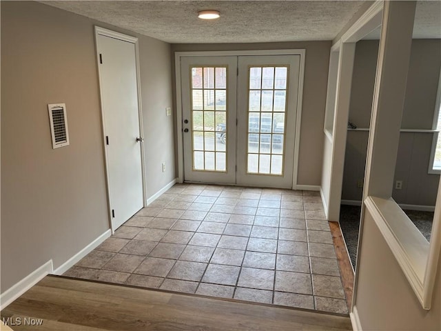 entryway featuring light tile patterned floors, baseboards, visible vents, and a textured ceiling