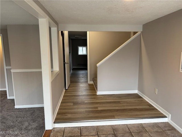 corridor featuring a textured ceiling, stairway, and baseboards