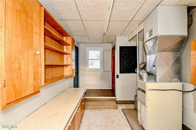 interior space featuring light tile patterned floors, a drop ceiling, heating unit, light countertops, and open shelves