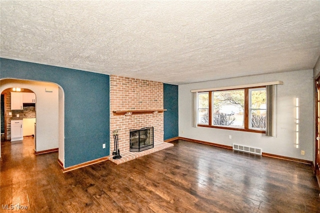 unfurnished living room with arched walkways, a fireplace, visible vents, wood finished floors, and baseboards