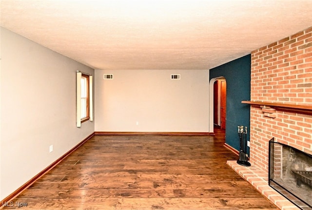 unfurnished living room featuring arched walkways, a brick fireplace, wood finished floors, and visible vents