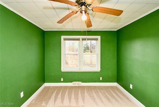 spare room with ceiling fan, carpet floors, visible vents, baseboards, and crown molding