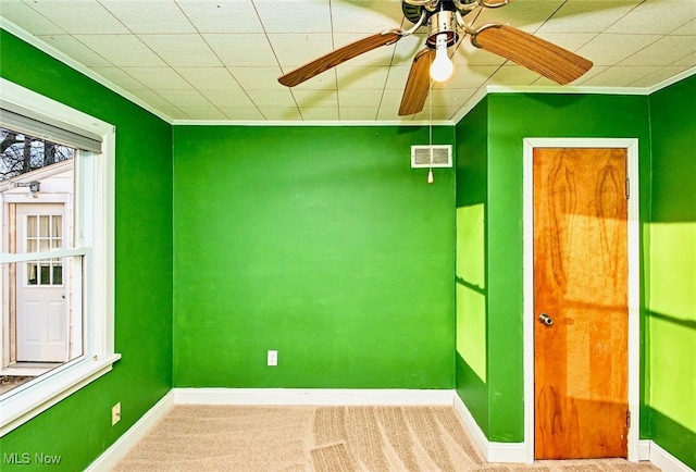 carpeted spare room with ornamental molding, visible vents, ceiling fan, and baseboards