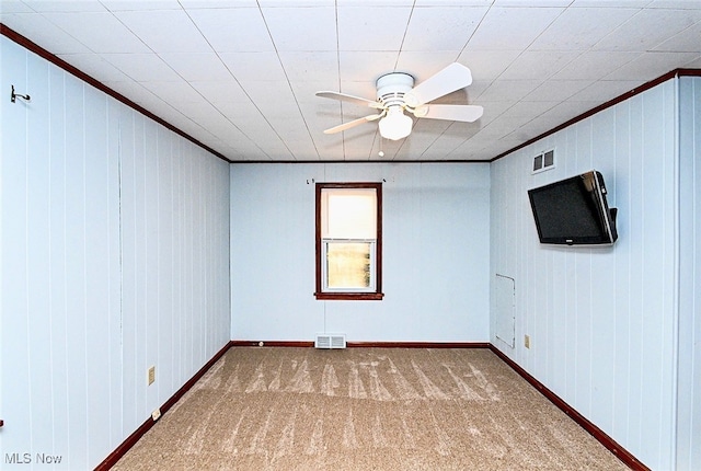 carpeted spare room with ceiling fan, ornamental molding, visible vents, and baseboards