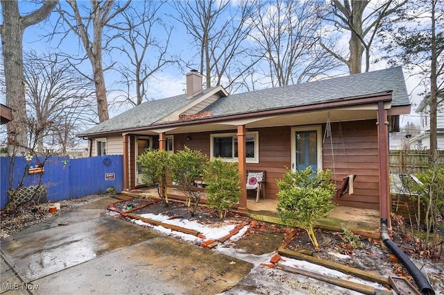 view of front of house featuring roof with shingles, a porch, a chimney, and fence