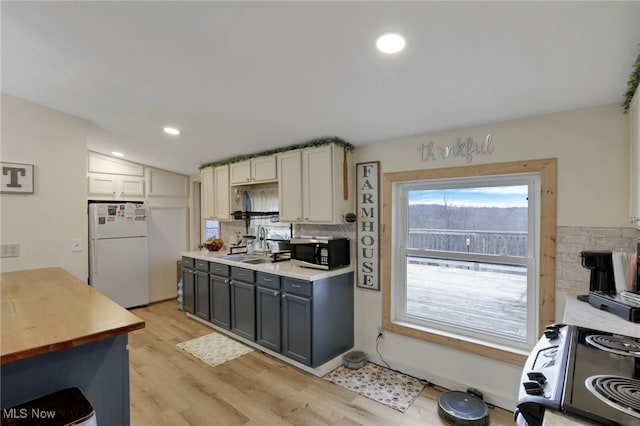 kitchen featuring light wood finished floors, stainless steel microwave, backsplash, freestanding refrigerator, and a sink