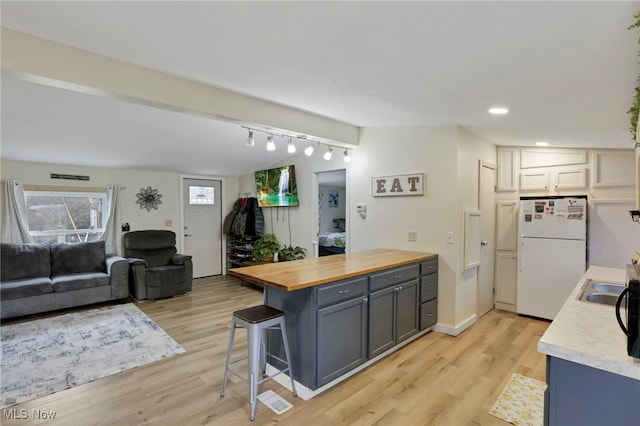 kitchen featuring butcher block counters, light wood-style flooring, freestanding refrigerator, a peninsula, and a kitchen bar