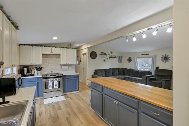 kitchen featuring wood counters, open floor plan, backsplash, stainless steel range oven, and a sink