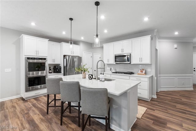 kitchen with a kitchen island with sink, stainless steel appliances, dark wood-type flooring, a sink, and decorative backsplash