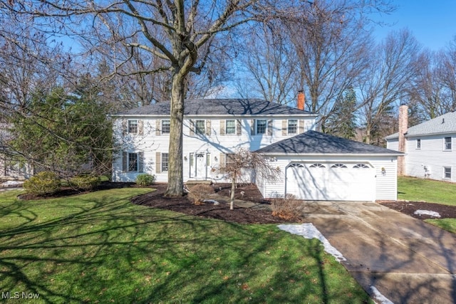 colonial-style house with a garage, a front yard, concrete driveway, and a chimney