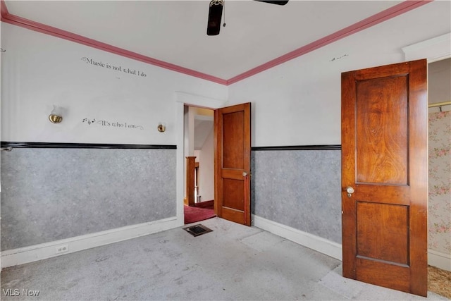 spare room featuring ceiling fan, a wainscoted wall, carpet floors, visible vents, and ornamental molding