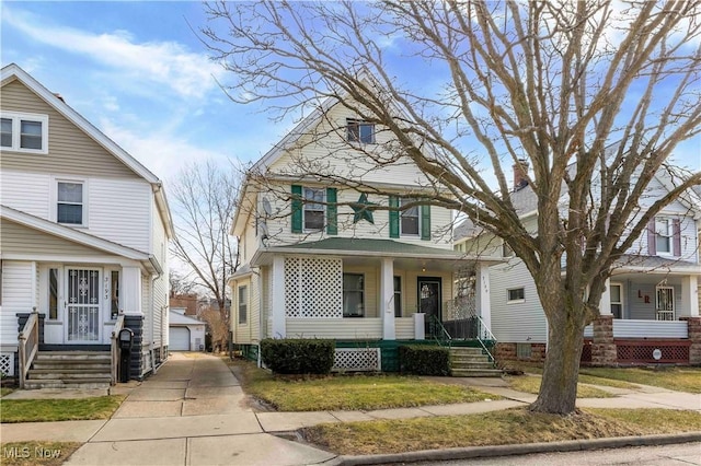 american foursquare style home with a detached garage, a porch, and an outbuilding