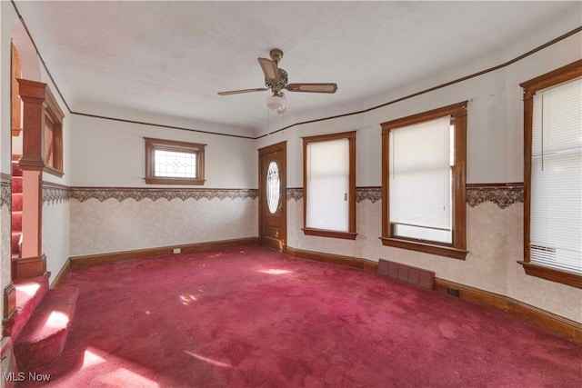 carpeted spare room featuring ceiling fan, a wainscoted wall, visible vents, baseboards, and wallpapered walls