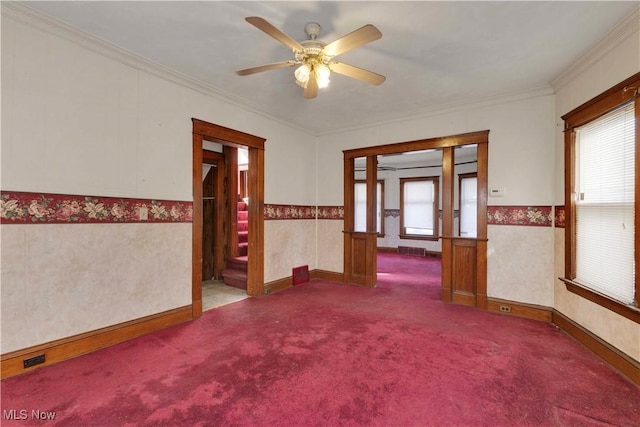 carpeted empty room with ceiling fan, baseboards, crown molding, and wainscoting