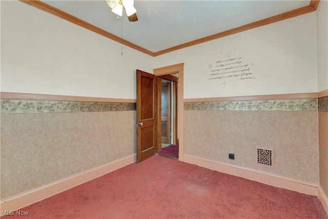 carpeted spare room featuring a ceiling fan, visible vents, ornamental molding, wainscoting, and wallpapered walls