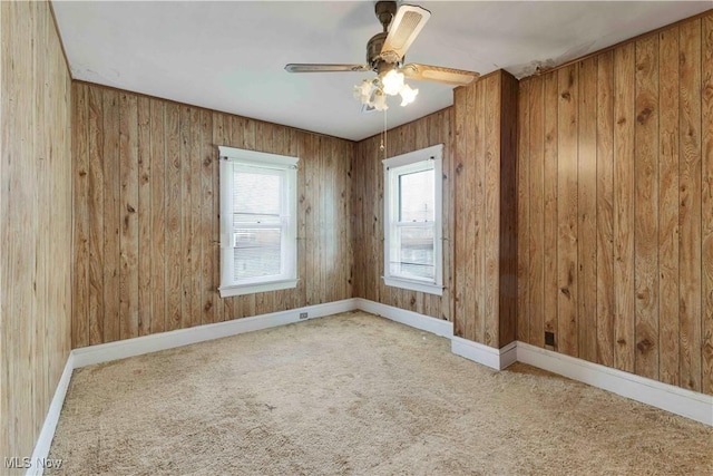 carpeted spare room with a ceiling fan, wooden walls, and baseboards