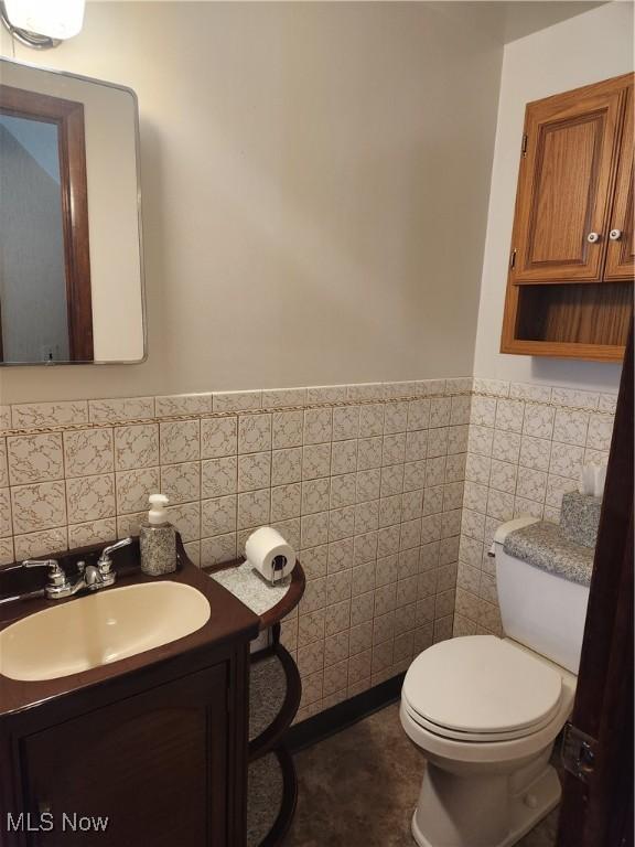 half bathroom featuring toilet, a wainscoted wall, tile walls, and vanity