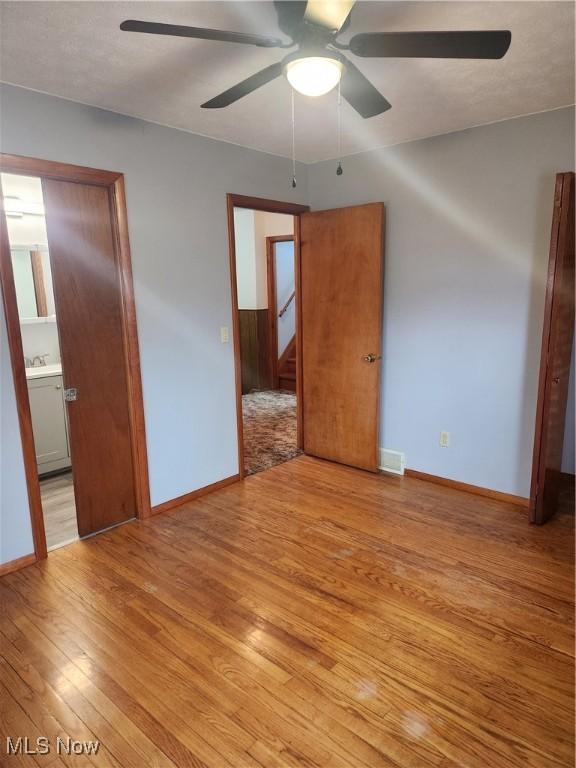 unfurnished bedroom featuring ensuite bathroom, a ceiling fan, baseboards, visible vents, and light wood-style floors