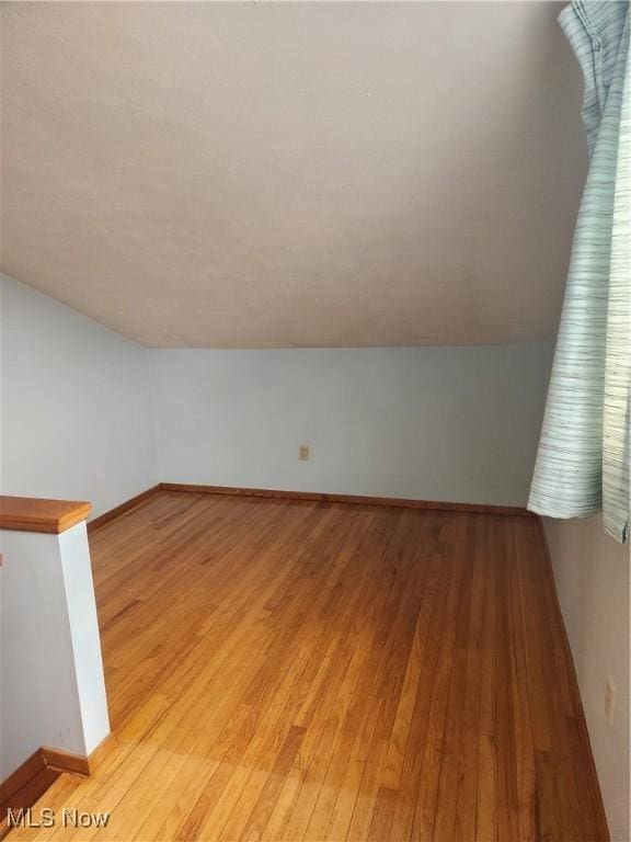 additional living space with light wood-type flooring, baseboards, and lofted ceiling