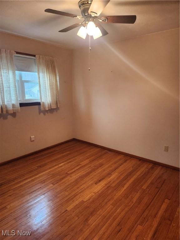 spare room featuring wood-type flooring, baseboards, and ceiling fan