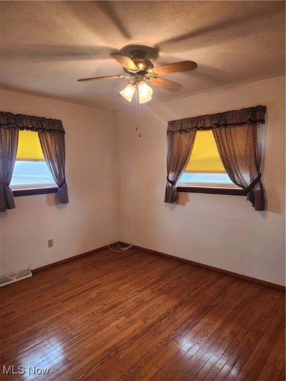 empty room with a textured ceiling, hardwood / wood-style floors, visible vents, and baseboards