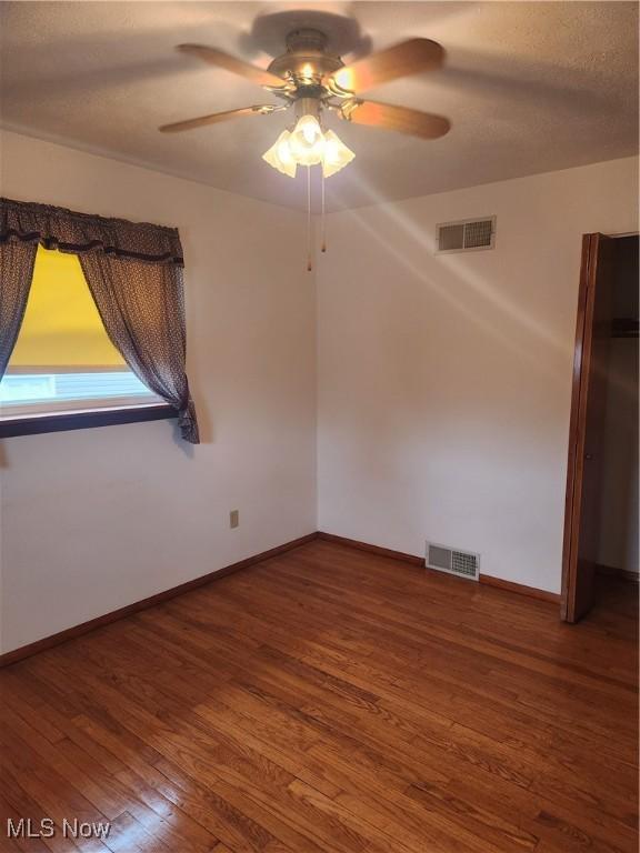 empty room with a ceiling fan, visible vents, baseboards, and wood finished floors