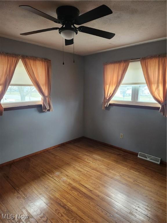 spare room with a textured ceiling, a ceiling fan, visible vents, baseboards, and hardwood / wood-style floors