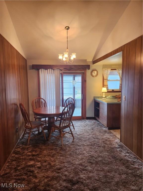 carpeted dining space with lofted ceiling, wood walls, and an inviting chandelier