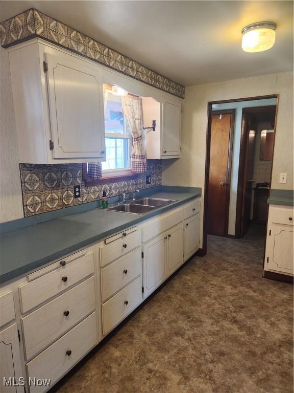 kitchen featuring dark countertops, white cabinetry, a sink, and decorative backsplash