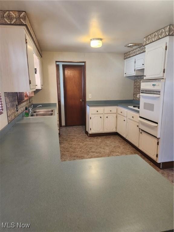 kitchen featuring tasteful backsplash, dark countertops, oven, a sink, and a warming drawer