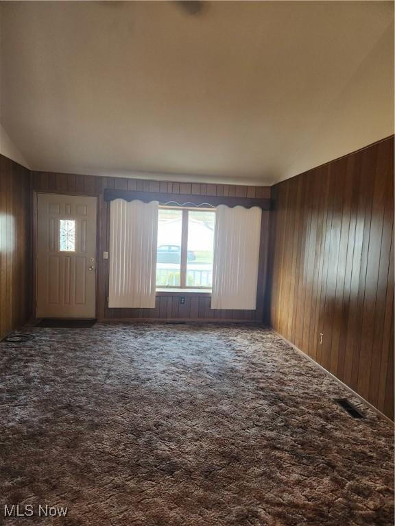 unfurnished living room featuring vaulted ceiling, carpet, and wooden walls