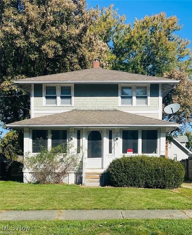 view of front facade with a shingled roof, a chimney, and a front yard