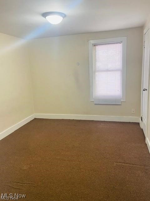 unfurnished room featuring dark carpet and baseboards