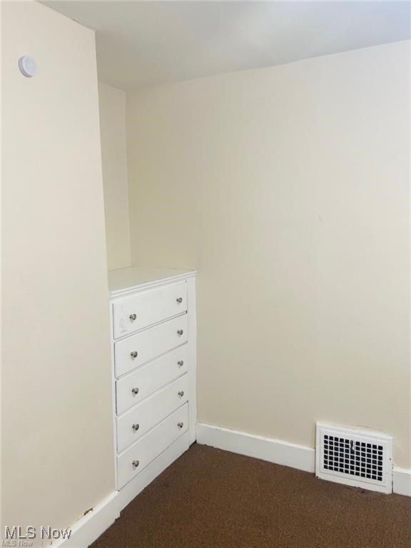 empty room with baseboards, visible vents, and dark carpet