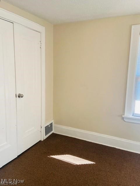 unfurnished bedroom with a closet, visible vents, dark carpet, and baseboards