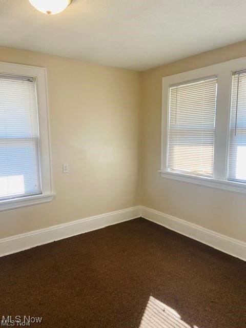 unfurnished room with a healthy amount of sunlight, baseboards, and dark colored carpet