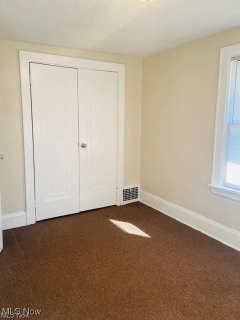 unfurnished bedroom with visible vents, baseboards, and dark colored carpet