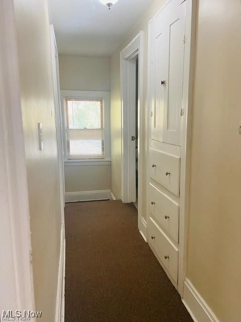 hallway featuring dark colored carpet and baseboards