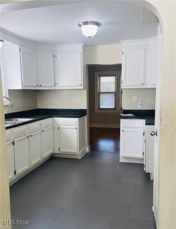 kitchen with dark countertops, white cabinetry, a sink, and arched walkways