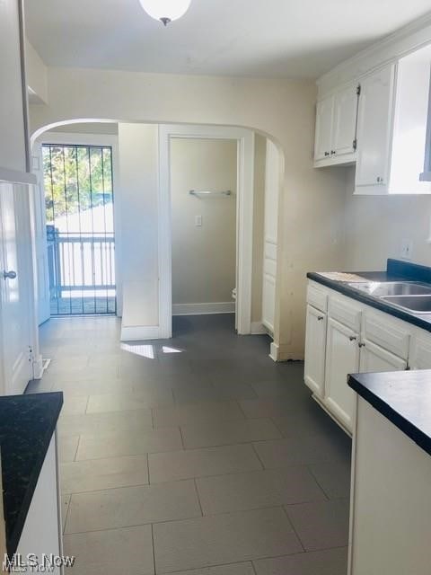 kitchen with arched walkways, white cabinets, a sink, and dark countertops