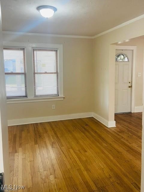 spare room featuring ornamental molding, baseboards, and wood finished floors