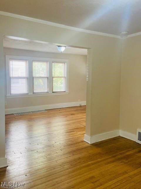 spare room with ornamental molding, wood finished floors, visible vents, and baseboards