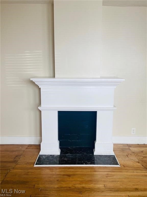 details featuring a fireplace with flush hearth, baseboards, and wood finished floors