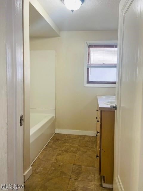 full bath featuring a washtub, baseboards, and vanity