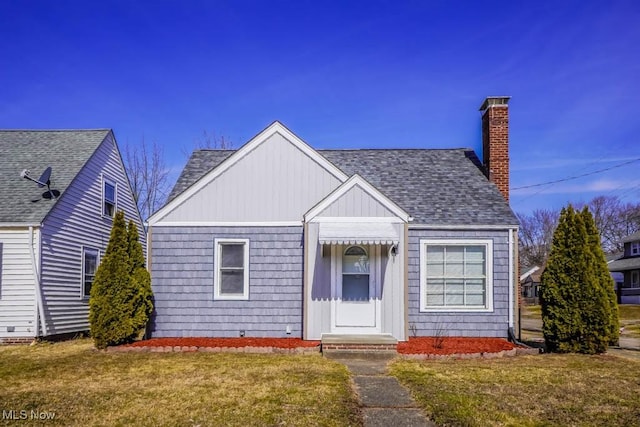 view of front facade featuring roof with shingles, a chimney, and a front yard