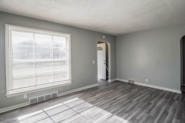 unfurnished room with arched walkways, a textured ceiling, dark wood finished floors, and visible vents