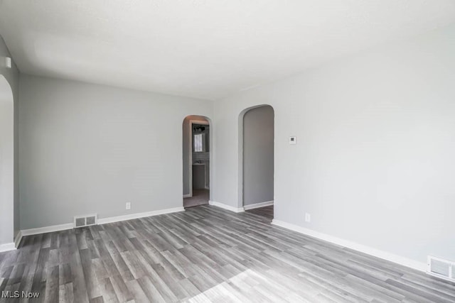 empty room featuring baseboards, visible vents, arched walkways, and wood finished floors