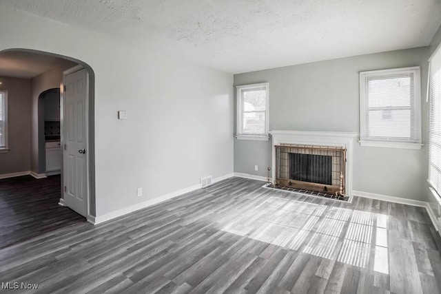 unfurnished living room with arched walkways, wood finished floors, a fireplace with flush hearth, and visible vents